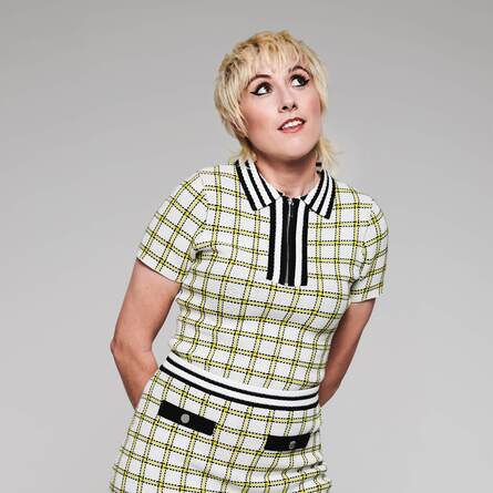 Maisie Adam against a grey background. She's wearing a white and light green checkered outfit and she has a happy expression.