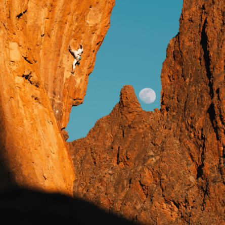 A person is climbing up orange coloured cliffs