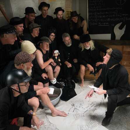 The Spooky Men’s Chorale looking over a hand-drawn map, plotting a plan