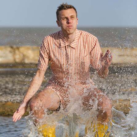Harry Baker in a onesie by the beach. He's being splashed with water