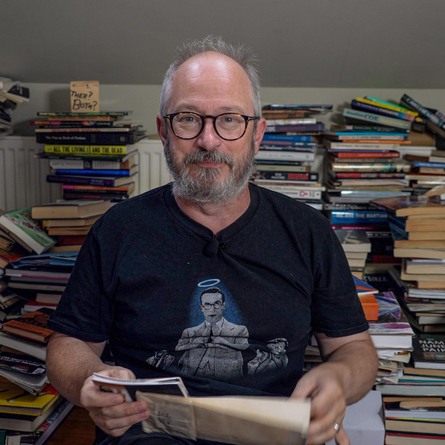 Robin Ince surrounded by stacks of books