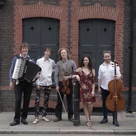 A photo of the band ZRI, they are holding their instruments and is standing in front  of a red brick building.